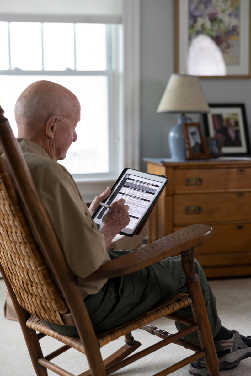 Elderly man reading tablet in rocking chair by window in cozy living room