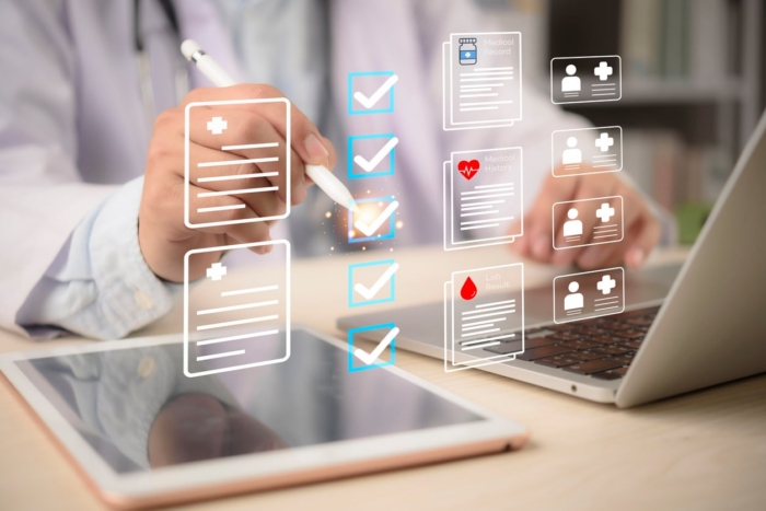 Doctor using digital checklist on tablet and laptop for medical records management