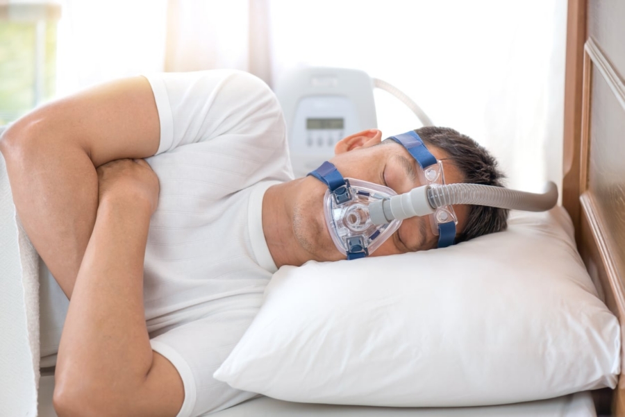 Man sleeping with a CPAP machine for sleep apnea therapy in a bright bedroom