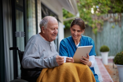 Elderly man and caregiver looking at tablet outdoors