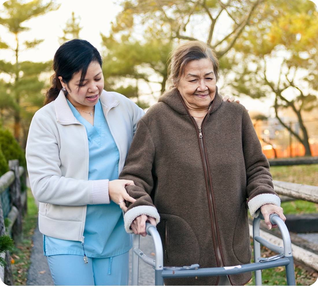 Caregiver assisting elderly woman with walker outdoors