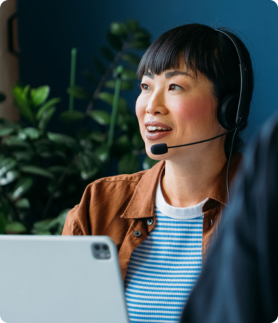 Smiling woman with headset using laptop in a modern office setting with plants