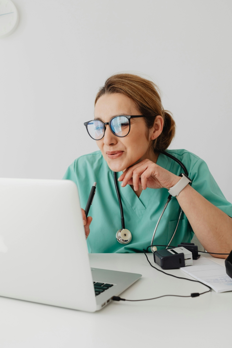 Female doctor in scrubs using laptop for telemedicine consultation