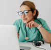 Medical professional in scrubs and glasses working on a laptop in an office setting
