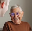 Elderly man with glasses smiling warmly at a younger person