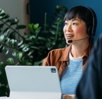 Woman with headset working on laptop in office with plants