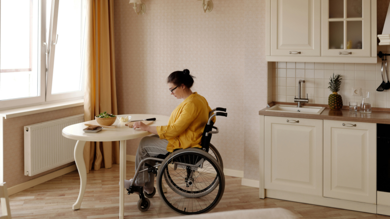 Woman in wheelchair using tablet at kitchen table in a cozy apartment