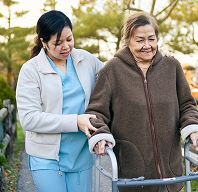 Caregiver assisting elderly woman with walker outdoors