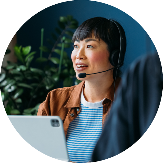 Woman wearing a headset working on a laptop in a plant-filled office.